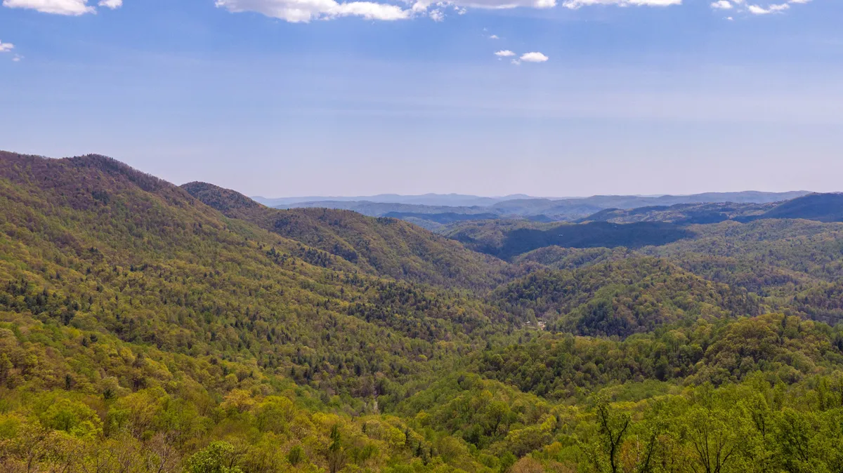 A sweeping view of lush green hills, distant mountains, and open sky, evoking the natural beauty of the Blue Ridge region. The scene suggests opportunities for hiking, exploring, and enjoying the outdoors.