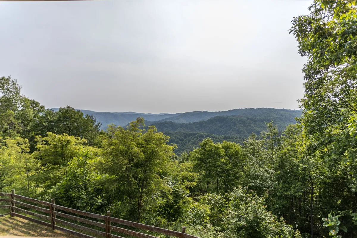 An open view of distant blue hills and lush greenery beyond a rustic wooden fence, capturing the sense of natural expanse. Perfect for picnics, hikes, and outdoor games in a private mountain setting.