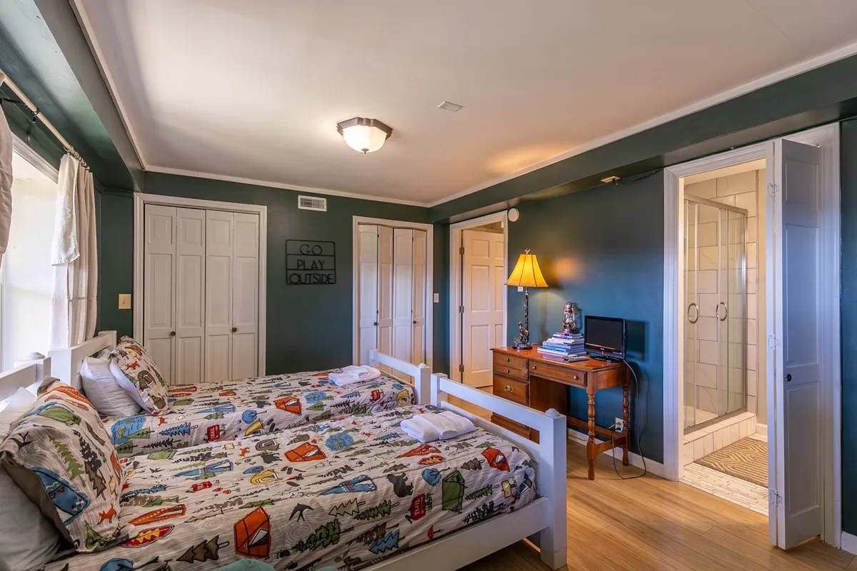 A playful bunk room featuring colorful bedding, a vintage desk with lamp, and a cheerful sign on the wall. The space is designed for sleeping, reading, and playing games, with a mood that is both playful and relaxed.