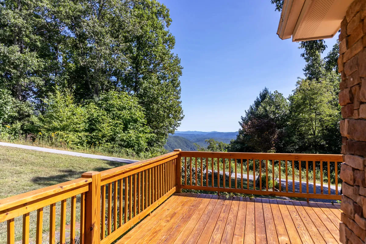 This image displays a wooden deck with outdoor seating, set against a backdrop of rolling mountains and green foliage. The serene setting is perfect for al fresco dining, grilling, or simply savoring the panoramic views after a day of adventure.