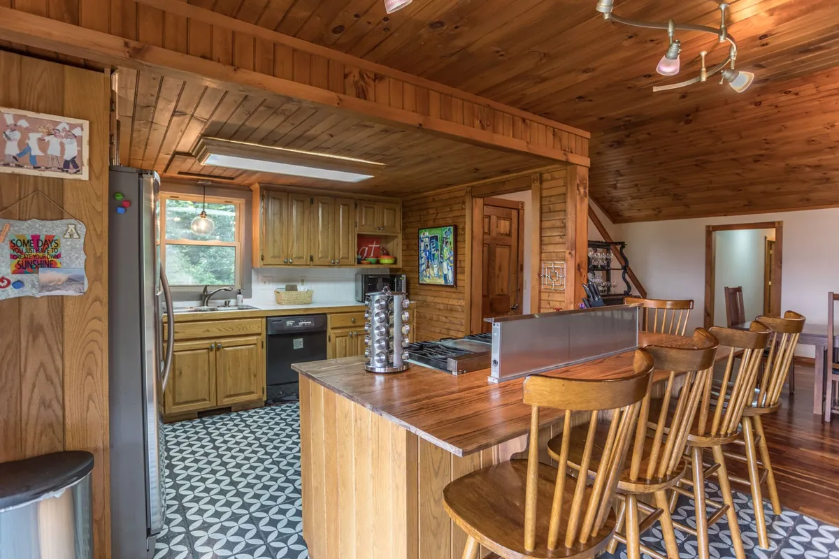 This image features the kitchen island surrounded by wooden cabinetry, decorative artwork, unique tile flooring, and bar stools, creating a cozy and welcoming environment. The space is designed for cooking, entertaining, and gathering.