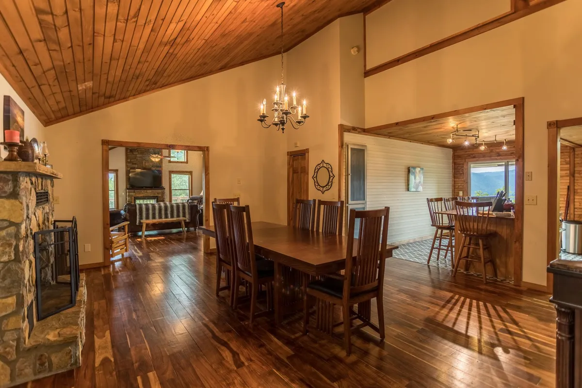 This image centers on a grand dining table beneath a chandelier, flanked by a glowing fireplace and set within an open-plan area that flows into the living space. The setting feels perfect for group meals, board games, and celebrations, with the open doorway hinting at seamless movement between gathering areas.