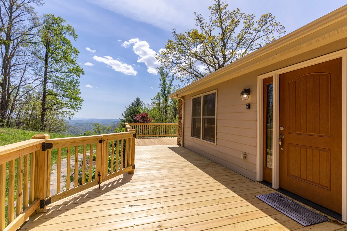 A wide wooden deck with comfortable seating facing dramatic mountain vistas. The foreground includes the welcoming front door, while the panoramic view stretches to the horizon—ideal for morning coffee or evening stargazing.